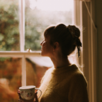 woman holding a mug of coffee standing next to a window looking out it with the blog post title stating "embracing a healthier digital relationship'