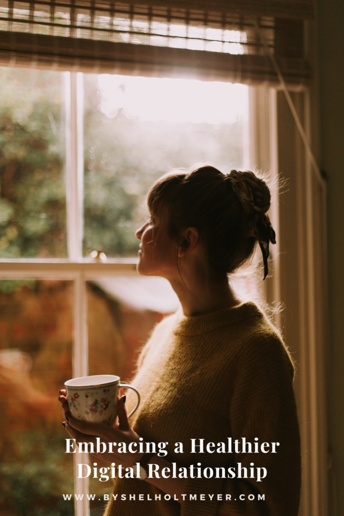 woman holding a mug of coffee standing next to a window looking out it with the blog post title stating "embracing a healthier digital relationship'