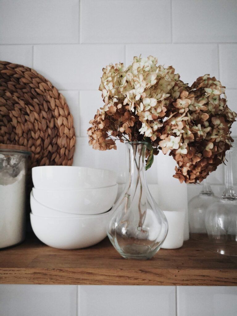 Neatly stacked bowls on a shelf with a jar of flour and a glass vase holding flowers.