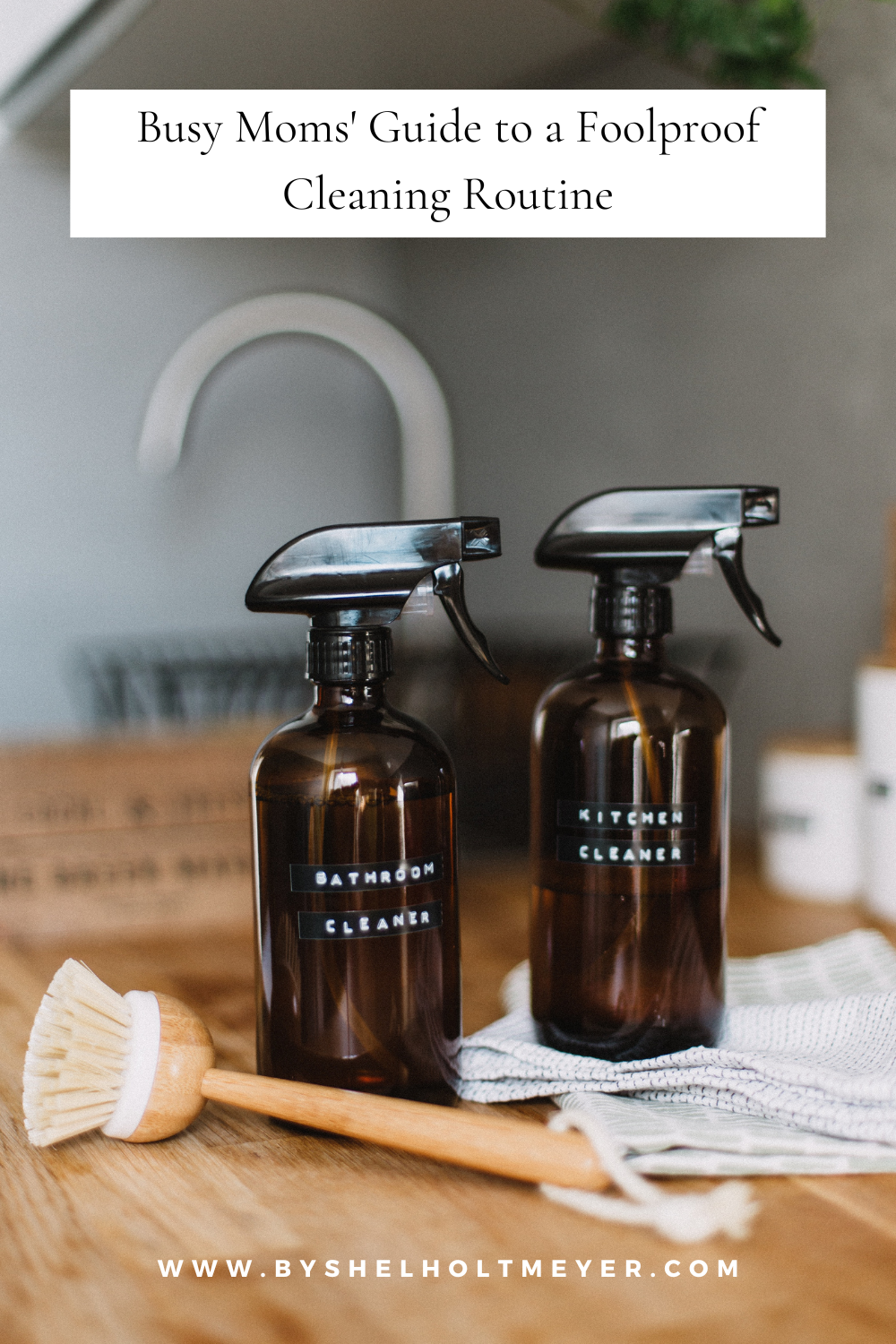 Cleaning bottles on a dish cloth with a brush beside them, and a sink in the background. The image features a text overlay with the blog title 'Busy Moms' Guide to a Foolproof Cleaning Routine.'