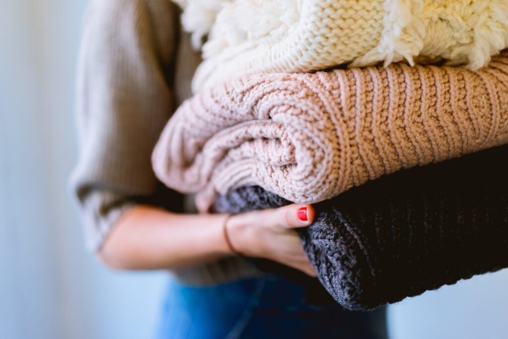 Close up of a stack of folded sweaters a woman in carrying.
