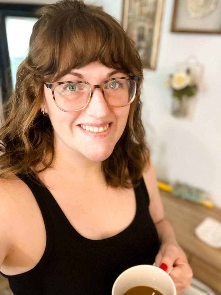 A portrait of the blogger (Shel Holtmeyer) holding a coffee cup, smiling warmly, with a cozy background.